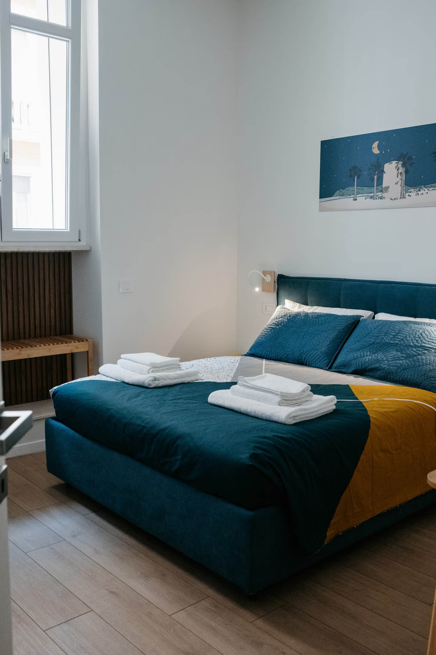Camera da letto matrimoniale con arazzo illustrato "luna e palme", panca in legno sotto la finestra e luce naturale dal cortile