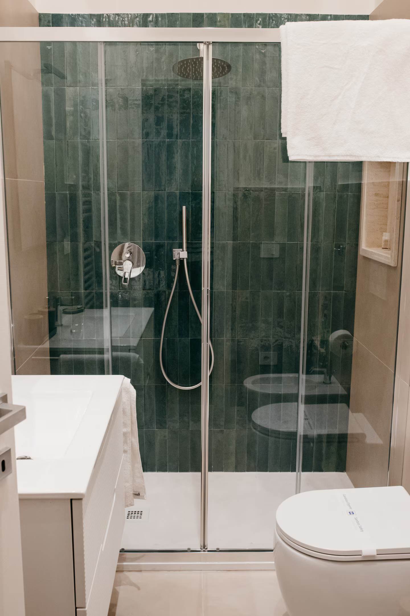 Bagno visto attraverso una porta socchiusa, piastrelle zellige verde scuro e asciugamano bianco