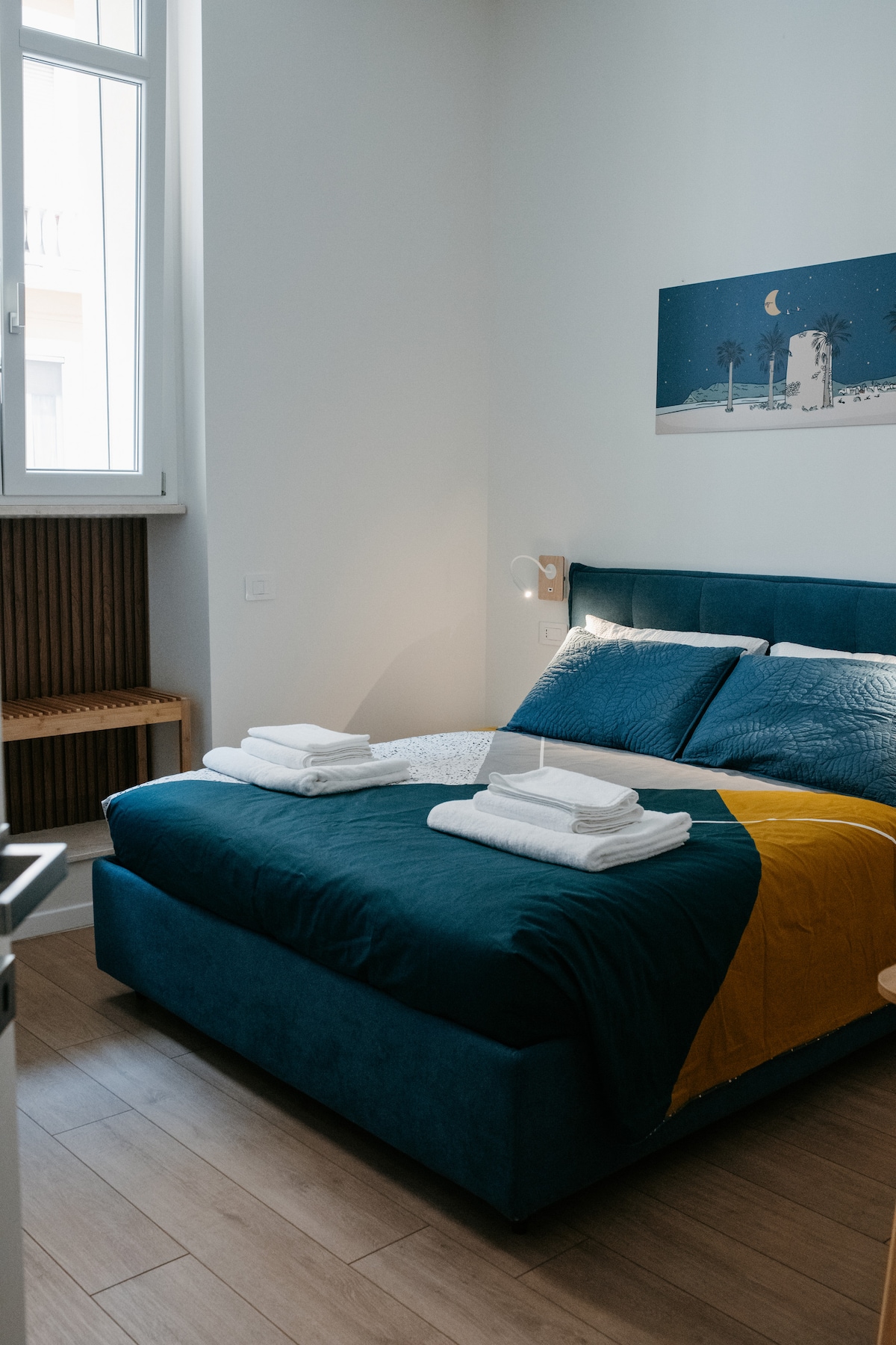 Camera matrimoniale con letto blu petrolio e quadro mediterraneo